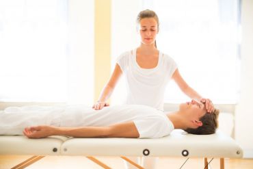 Eine Reiki Anwendung wird im DHANANJAYA in Chemnitz angezogen auf dem Massagetisch durchgeführt